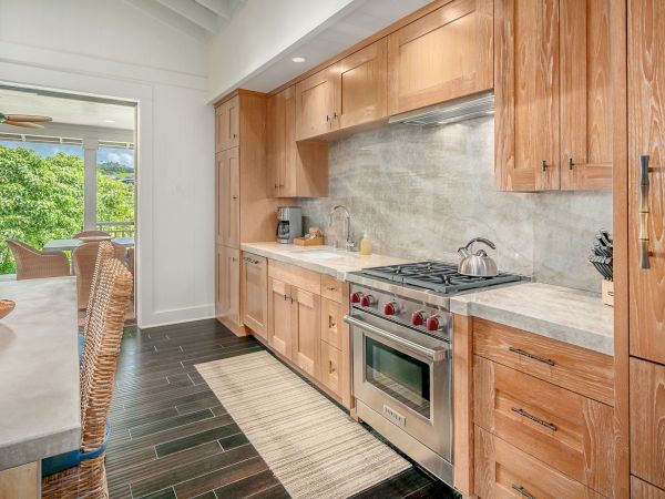 A modern kitchen with wood cabinetry, a marble-look backsplash, stainless range, double sink, and a view to greenery through the window.