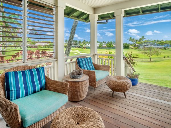 A breezy porch with wicker seating and blue cushions, overlooking a lush golf course and palm-lined tropical view.