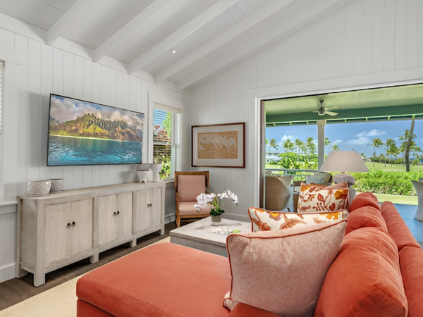 A bright, airy living room with orange sofas, a coffee table, and large windows overlooking greenery, in a covered veranda.