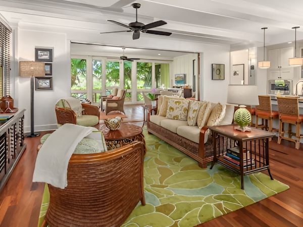 A bright living room with seating, a green patterned rug, pendant lights, and a small kitchen with stools and counters.