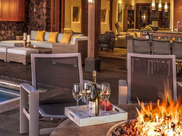 A luxury resort patio with a fire pit, wine glasses and bottle, lounge seating, and a swimming pool.
