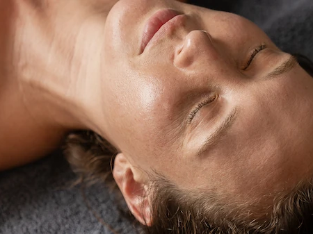 A man with eyes closed lying on a massage table, as a hand rests gently on his head in a relaxing spa moment.