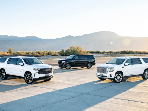 Three white SUVs parked on a concrete airstrip at sunset with distant mountains in the background.