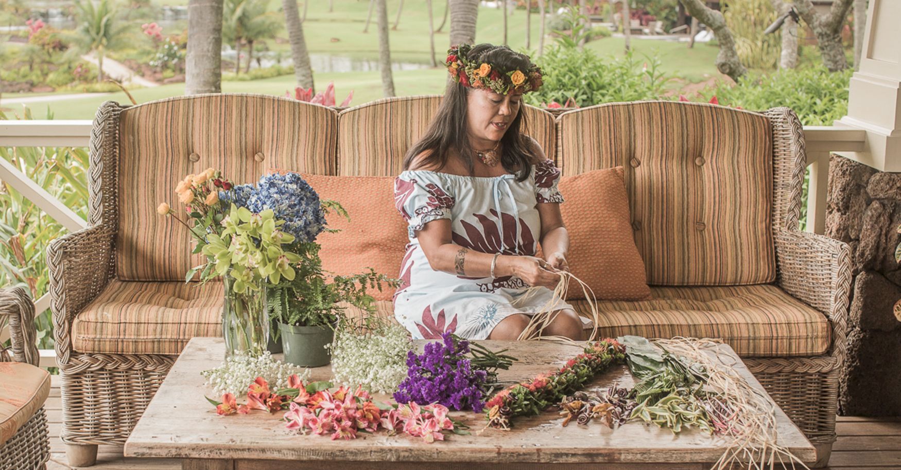 A woman arranging colorful flowers on a rustic outdoor sofa set, surrounded by fresh bouquets and greenery.