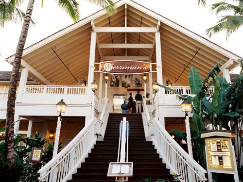 A sunny beach building with palm trees and wide stairs leading to Merriman&rsquo;s entrance.