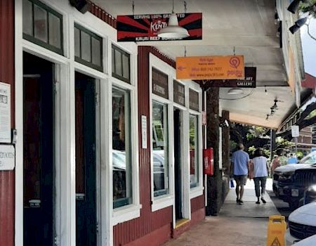 A covered street with storefront windows and signs, where a few people walk past parked cars.