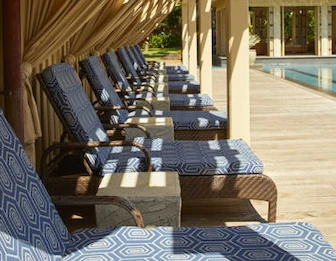 Outdoor patio by a pool with neatly arranged blue-and-white lounge chairs and patterned cushions, ready for relaxing afternoons.