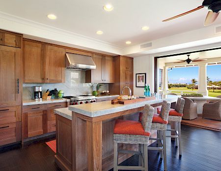 Sunlit outdoor-style kitchen with wood cabinets, an island, a ceiling fan, and open doors to a lush green yard.