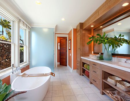 Bright modern bathroom with a freestanding tub, double sink vanity, warm wood cabinets, large windows, and a leafy plant display.