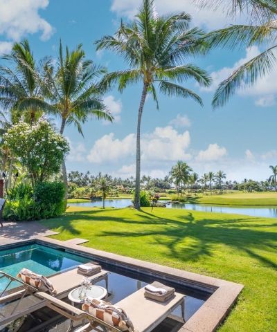 A backyard pool overlooks a lush golf course with palm trees and a lake under a bright blue sky.