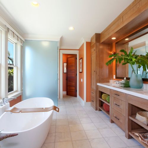 Bright modern bathroom with wood vanity, double sinks, a big tub, window light, and tropical plants in a clean, tiled space.