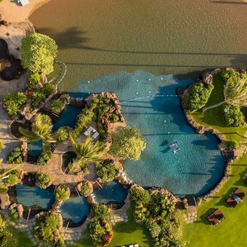 An aerial view of a tropical resort with winding pools, lush gardens, and sun loungers around palm-lined pathways.