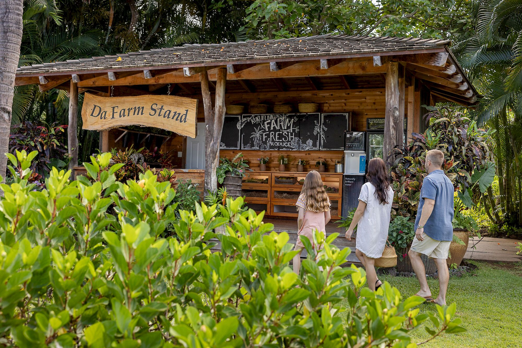 A &ldquo;Da Farm Stand&rdquo; in a lush tropical garden, with visitors walking past plant-filled stalls.